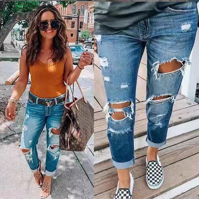 Women's blue mid-waist ripped denim jeans with distressed and washed details, casual pencil style pants.