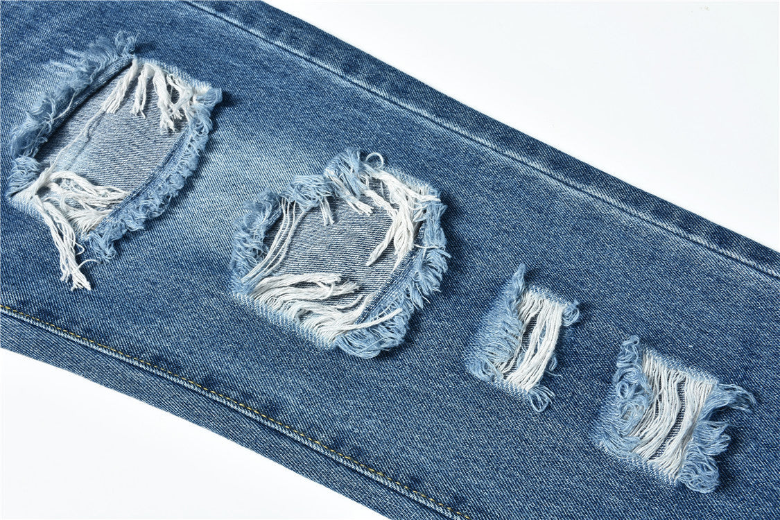 Close-up of distressed ripped blue denim jeans with frayed holes for women