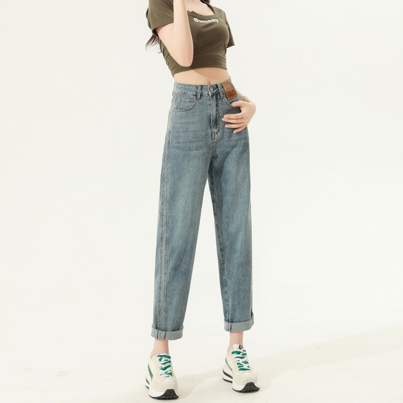 Woman wearing high waist straight harem jeans in retro blue denim with rolled cuffs and green-accented white sneakers.